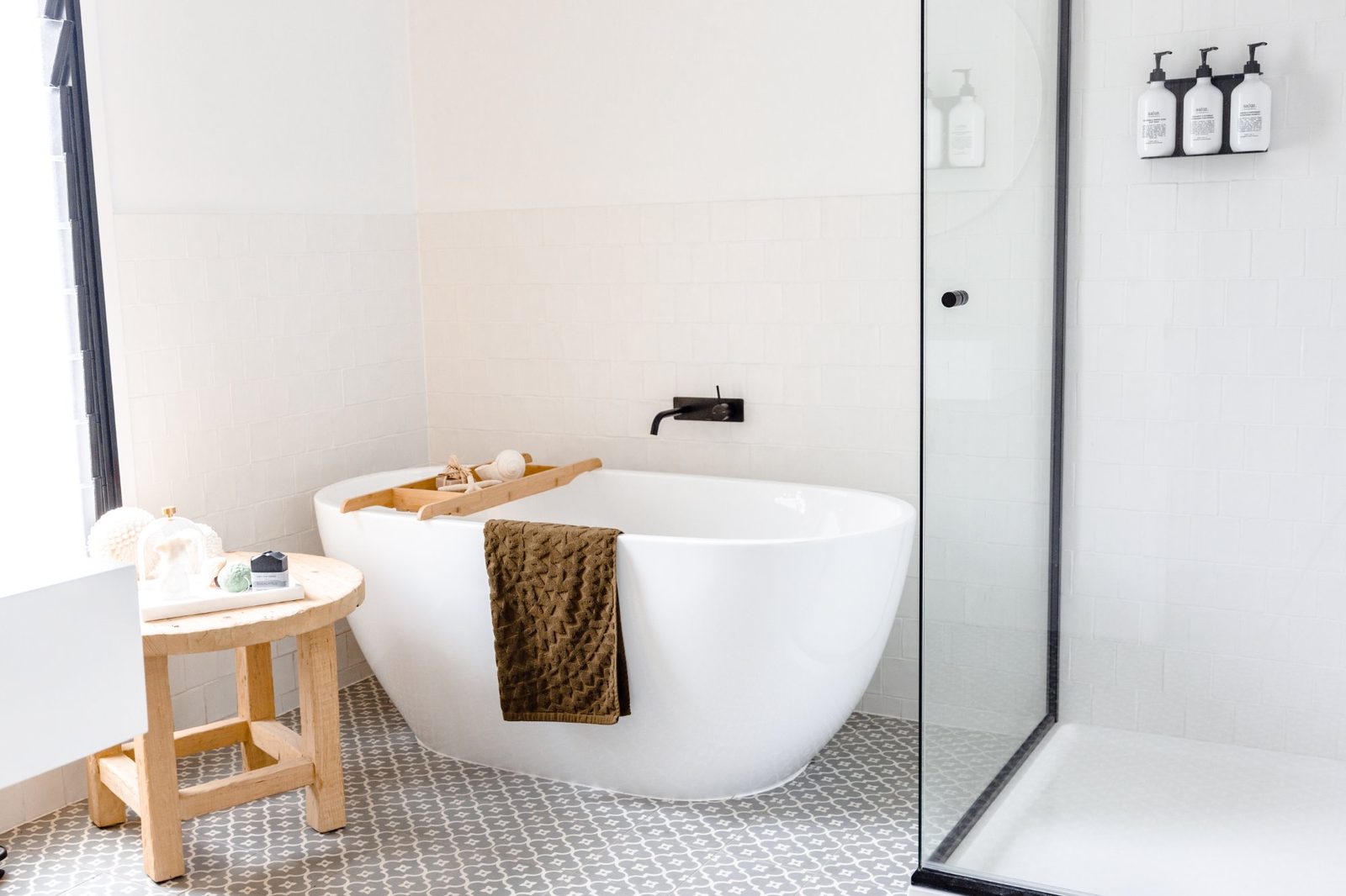 Luxe spa bathroom with freestanding bathtub, timber stool, patterned floor tiles and black tapware